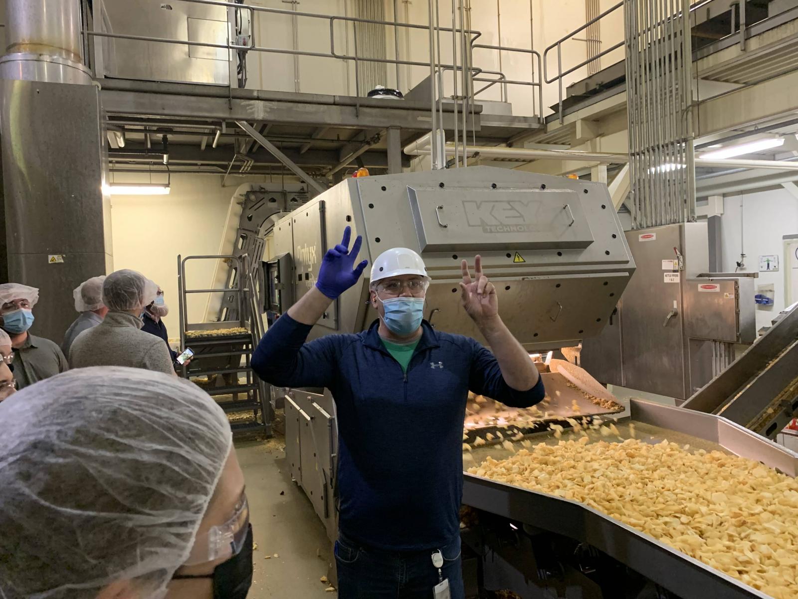 LEAD 39 student posing in front of conveyor belt loaded with potato chips.
