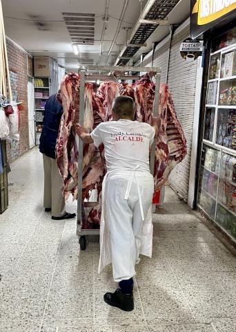 A worker pushes a rack of meat.