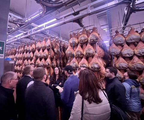 A group photo in front of racks of curing hams.