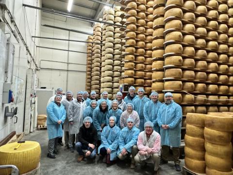 Lead group on a dairy tour in front of wheels of cheese.